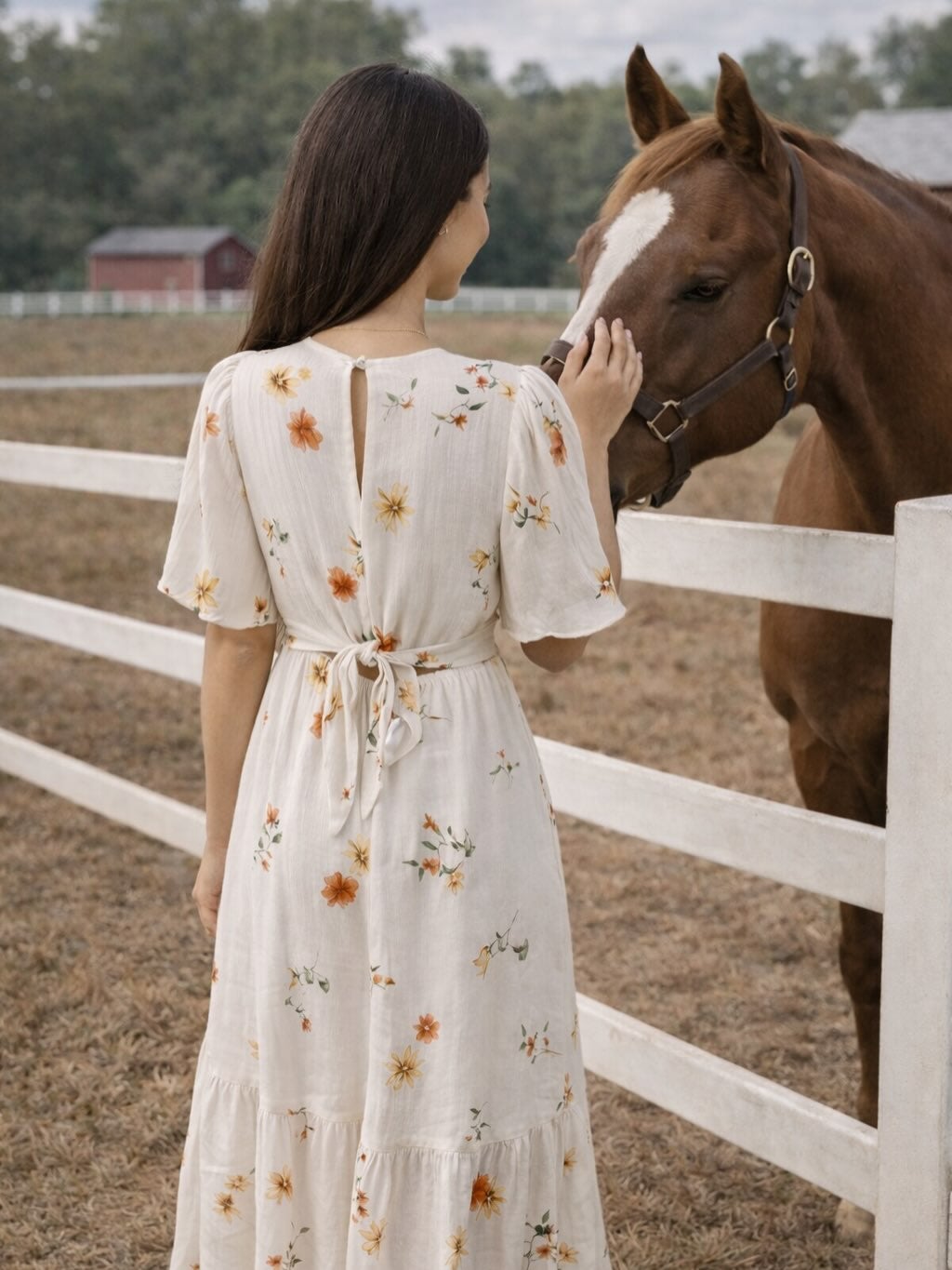 Woman wearing a flowy floral Room 34 maxi dress petting a horses head